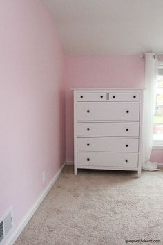 a white dresser sitting in the corner of a room with pink walls and carpeted floor