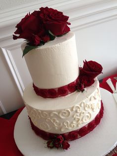 a three tiered wedding cake with red roses on the top and bottom, sitting on a white plate