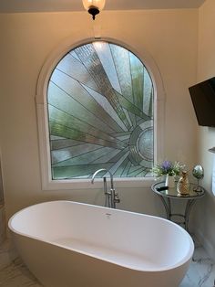 a bath tub sitting under a window next to a table with a vase on it