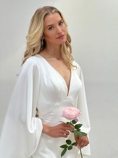 a woman in a white dress holding a pink rose