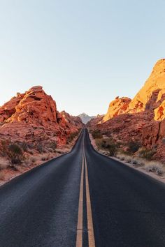 an empty road in the middle of desert with red rocks on both sides and blue sky above