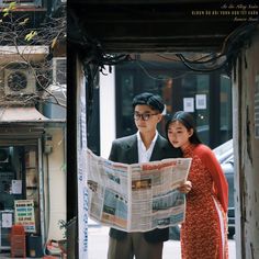 a man and woman standing next to each other while looking at a news paper in front of them