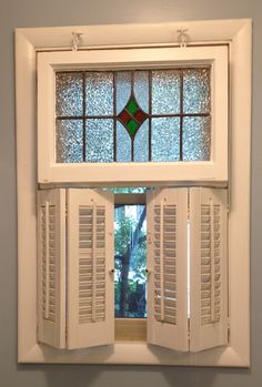 an open window with white shutters and green stained glass in the top half is shown