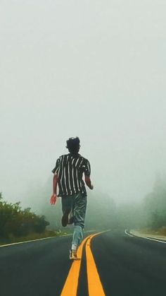 a man running down the middle of an empty road on a foggy day with trees in the background