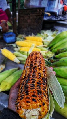 a person holding a corn on the cob in their hand with other food items nearby