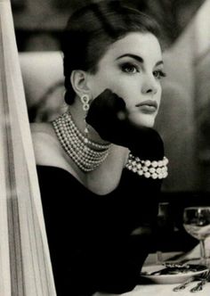 a woman sitting at a table wearing pearls