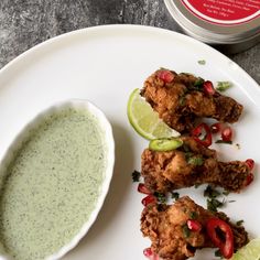 some food is on a white plate next to a bowl of green sauce and a lime wedge