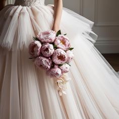 a woman in a wedding dress holding a bouquet of pink peonies and roses