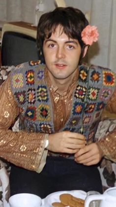 a man sitting at a table with food in front of him and flowers in his hair