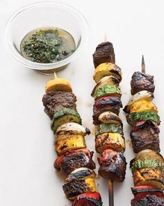 grilled meat and vegetable kabobs on skewers next to dipping sauce