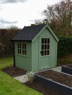 a small green shed sitting on top of a lush green field next to a garden