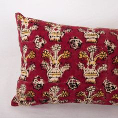 a red pillow with yellow and black flowers on the front, sitting on a white surface