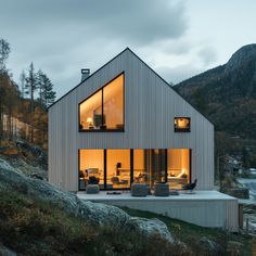 a modern house on the side of a mountain with windows lit up in the evening