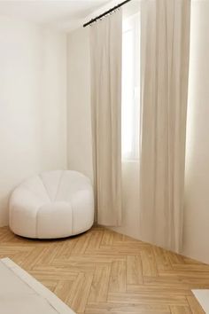 an empty room with a white round chair in front of a window and wooden parquet floor