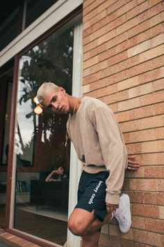 a young man leaning against a brick wall