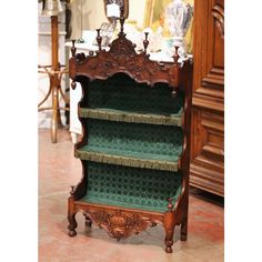 an ornate wooden shelf with green fabric on the top and bottom shelves, in front of a mirror