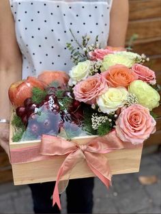 a person holding a box with fruit and flowers in it