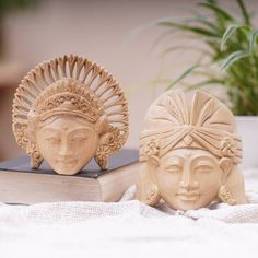 two ceramic head sculptures sitting on top of a white cloth next to an open book