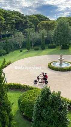 two people sitting on a scooter in the middle of a circular garden area