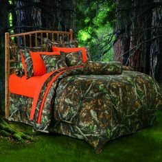 an image of a bed with camo comforter and orange pillows in the woods