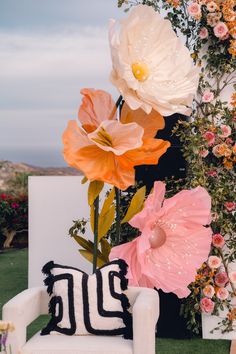 three large flowers sitting on top of a white chair in front of a flower covered wall