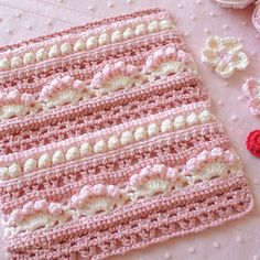 a crocheted pink and white blanket next to some doily on a table