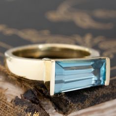 This is probably our favorite way to set a tapered baguette-shaped gemstone! An equally tapered ring setting, which follows the width of the stone that sits in the center. We find it to be so charming, so unique and incredibly elegant on the finger. The baguette has gorgeous spread across the top of one's finger, especially in this delicious blue shade. This aquamarine is crisp and chunky in the best way - the color combo of blue and yellow is also to die for! 18kt yellow gold Size 6 & resizable Modern Baguette Cut Topaz Promise Ring, Faceted Emerald Cut Topaz Ring In Fine Jewelry, Faceted Emerald Cut Topaz Fine Jewelry Ring, Emerald Cut Faceted Topaz Ring In Fine Jewelry Style, Baguette Cut Topaz Promise Ring, 14k Gold Baguette Cut Topaz Ring, Gift Blue Topaz Ring With Baguette Cut, Blue Topaz Baguette Cut Ring, Baguette Cut Blue Topaz Ring