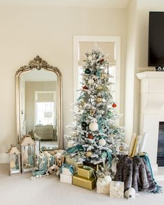 a decorated christmas tree in front of a fireplace with presents under it and a mirror on the wall