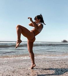 a woman doing yoga on the beach with her leg up and one leg in the air