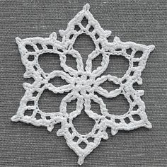 a white crocheted doily is shown on a gray surface, with the center piece in the shape of a snowflaket