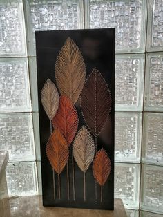 an art piece is displayed in front of glass block wall with four different colored leaves on it