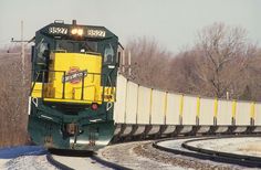 a yellow and green train traveling down tracks next to a snow covered field with trees