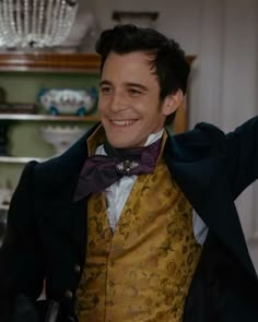 a man in a yellow vest and bow tie smiles while holding his arms up to the side