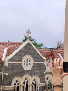 a person holding up their cell phone in front of a building with a cross on it