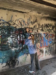 a woman standing in front of a graffiti covered wall with her hand up to her face