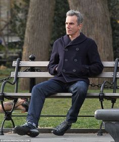 a man sitting on top of a wooden bench next to a park filled with trees