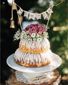 a cake with icing and flowers on top is sitting on a tree stump in the woods