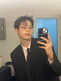 a man in a suit taking a selfie with his cell phone while wearing glasses