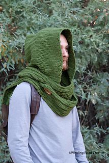 a man wearing a green knitted hood with his face covered by a scarf in front of some trees