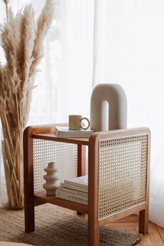 a table with some books and a cup on it next to a vase filled with dry grass