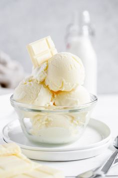 two scoops of vanilla ice cream in a glass bowl on a white plate with silverware