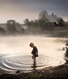 a young boy standing in the middle of a lake