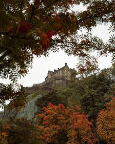 an old castle sits on top of a hill surrounded by trees and fall foliage in the foreground