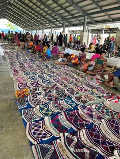 many people are sitting on the floor covered in colorful blankets and rugs as they wait for their turn