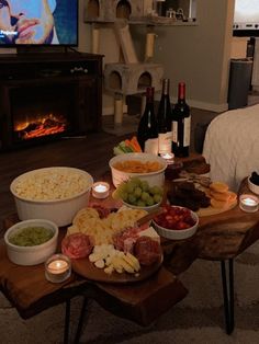 a wooden table topped with bowls of food next to a fire place filled with bottles of wine