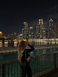 a woman is looking at the city lights from across the water in front of her