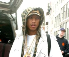 a young man wearing a hoodie and carrying a suitcase walks down the street in front of an suv