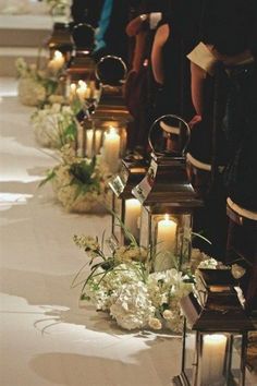 rows of lanterns with flowers and candles lined up on the aisle for a wedding ceremony