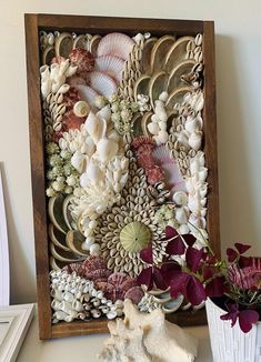 an art piece made out of seashells and flowers on a shelf next to a potted plant