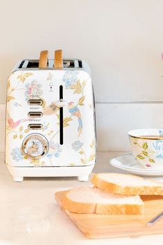 a white toaster sitting on top of a counter next to a cup and saucer